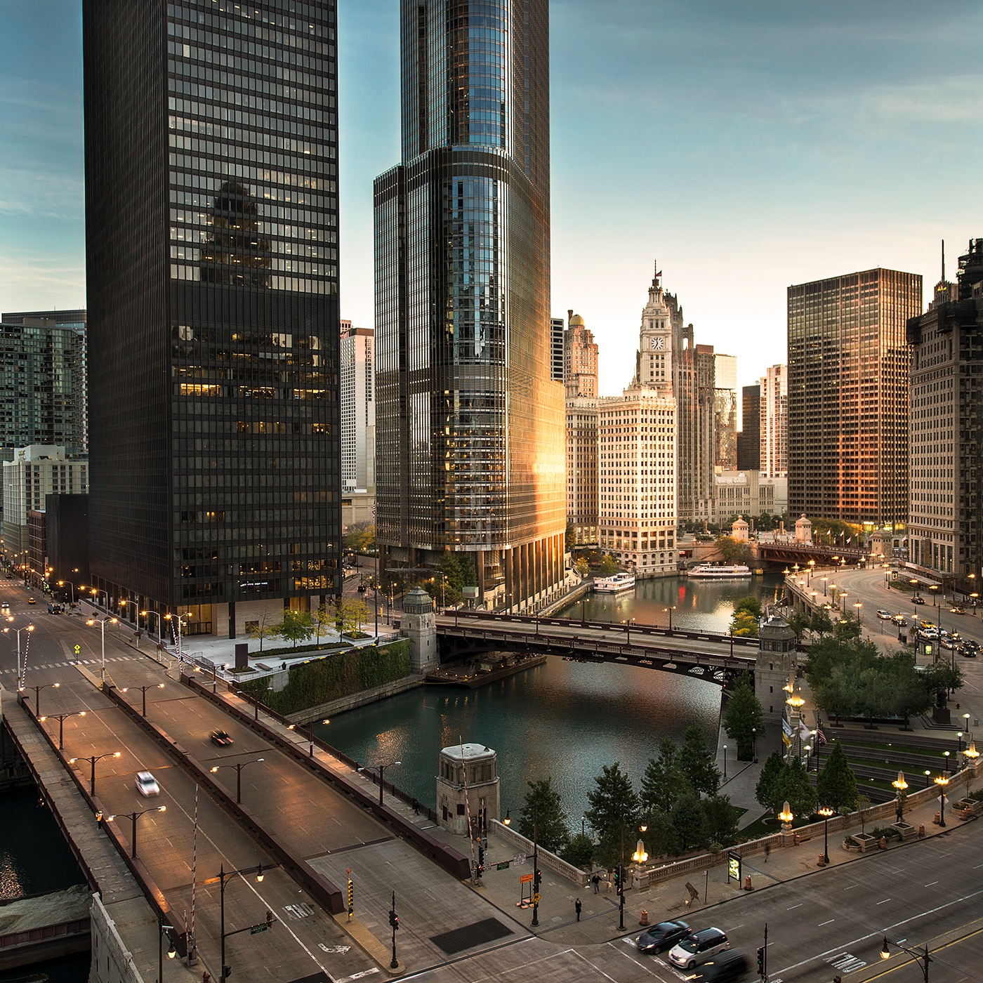 A stunning view of downtown Chicago at dusk, featuring the Chicago River and skyscrapers. The image captures illuminated bridges, modern glass buildings reflecting the fading sunlight and the bustling city streets with cars and pedestrians.