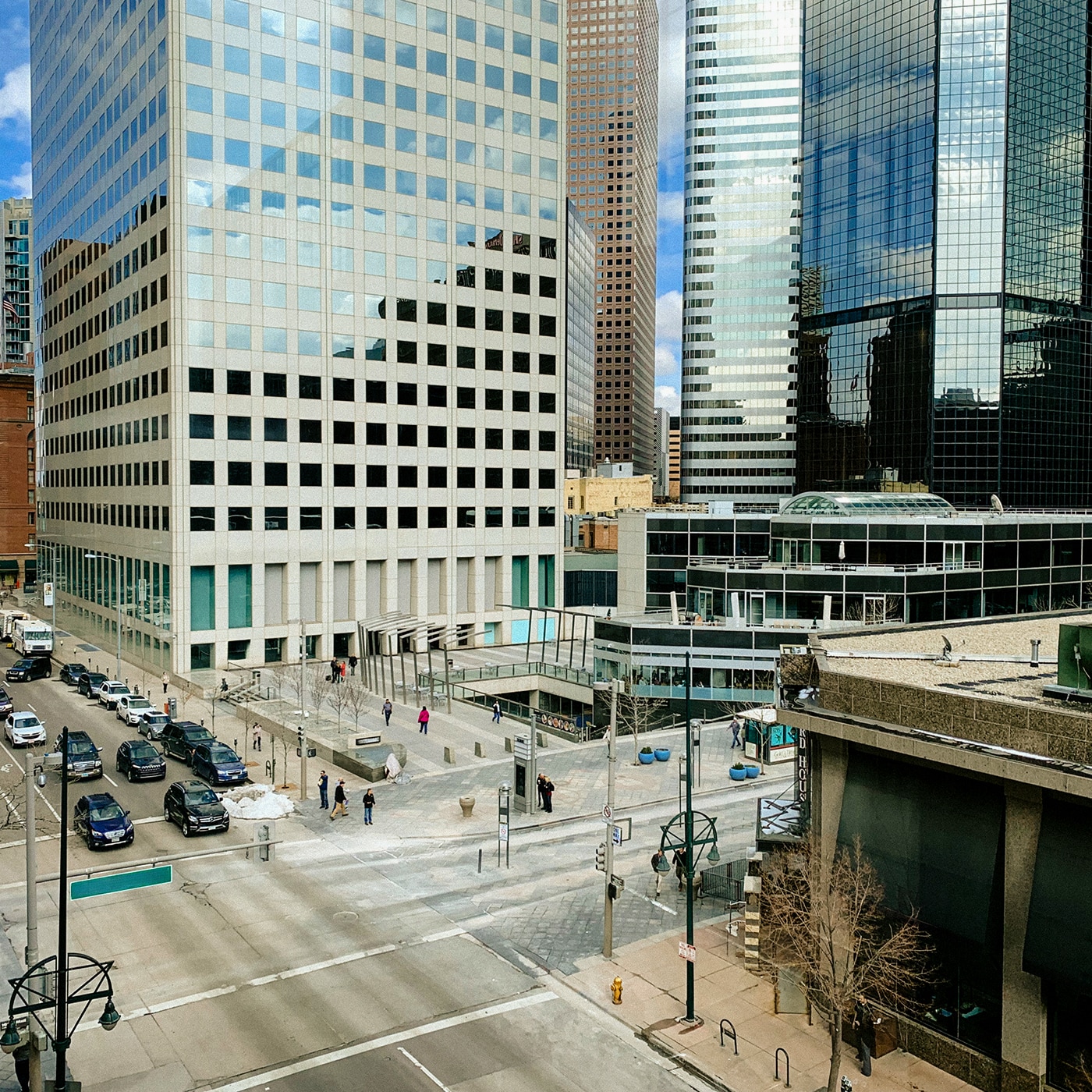 A worm-eye view of towering skyscrapers with reflective glass facades converging toward a bright blue sky with scattered clouds. The image is framed by a circular structure in the foreground