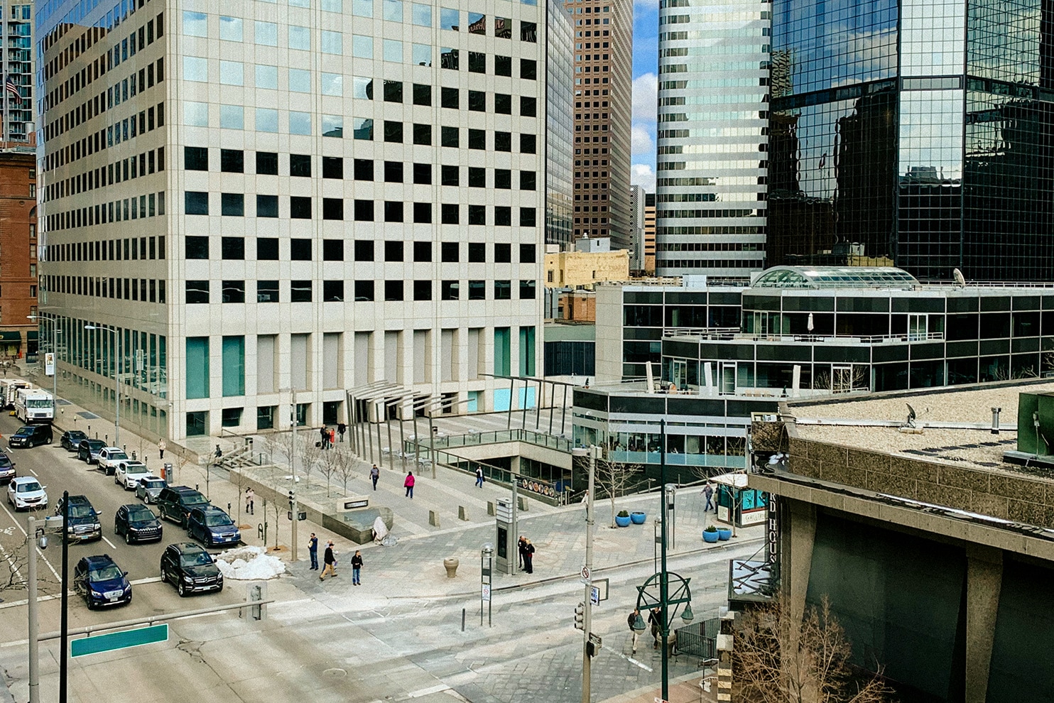 A worm-eye view of towering skyscrapers with reflective glass facades converging toward a bright blue sky with scattered clouds. The image is framed by a circular structure in the foreground