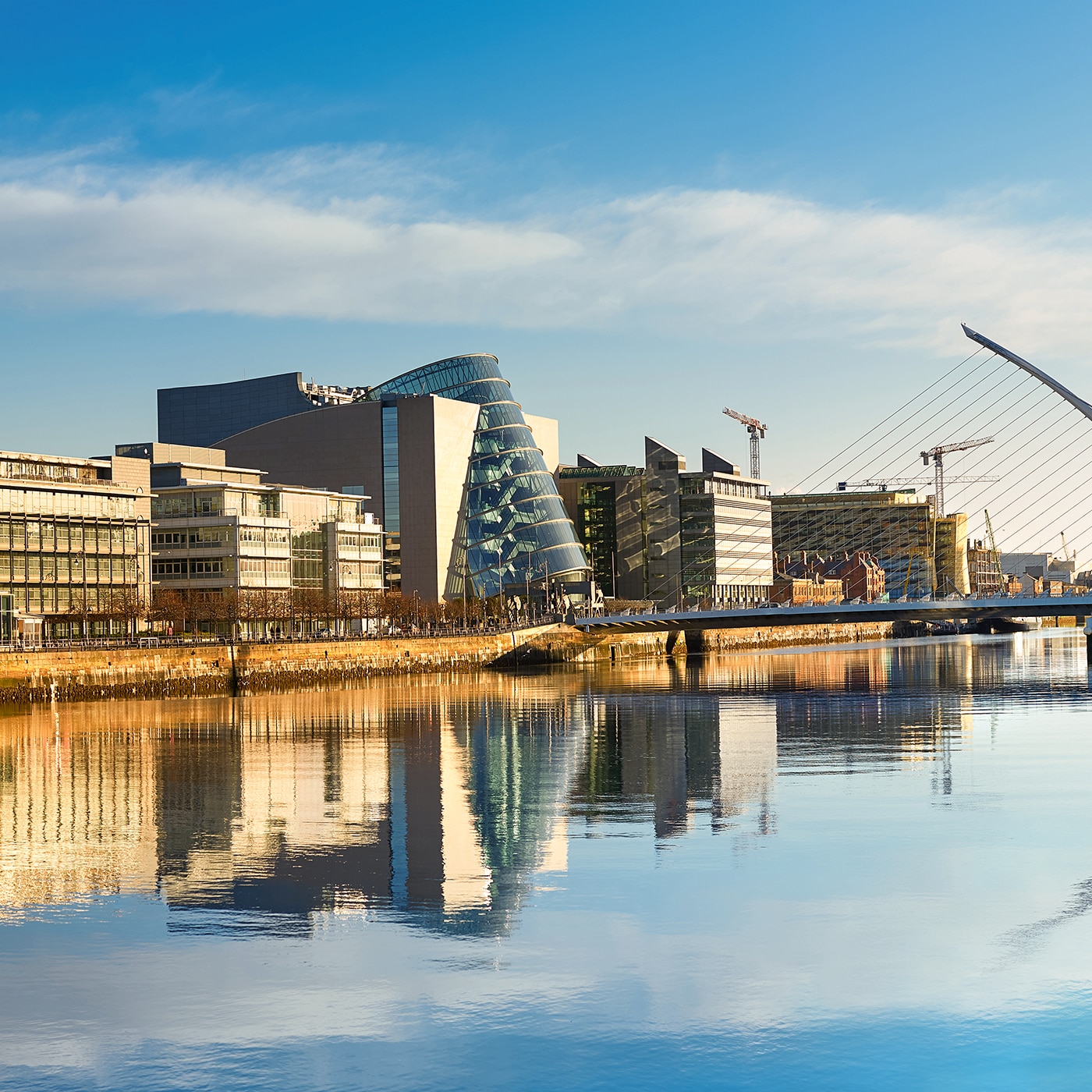 Modern buildings and the Samuel Beckett Bridge reflecting on the River Liffey in Dublin.