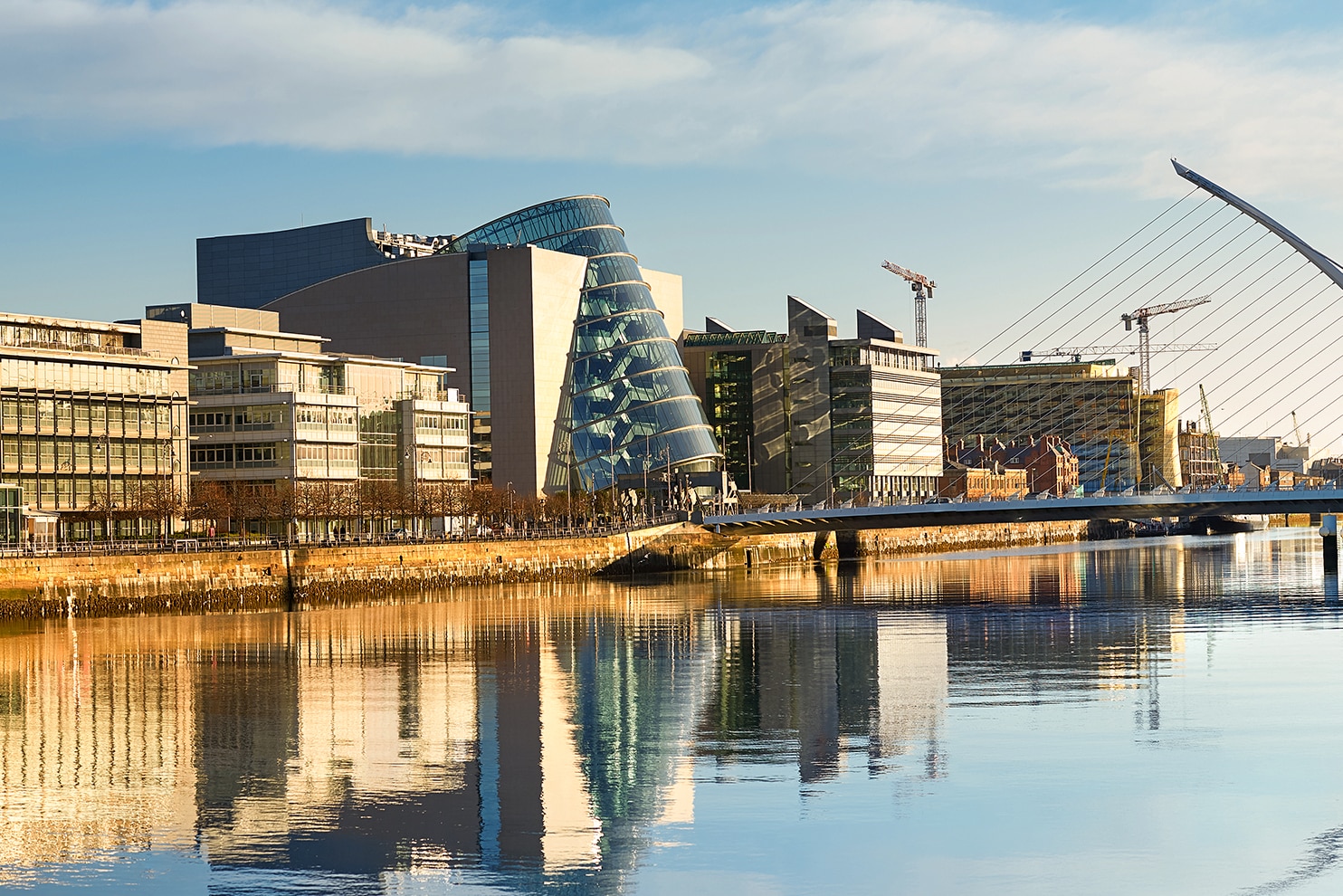 Modern buildings and the Samuel Beckett Bridge reflecting on the River Liffey in Dublin.