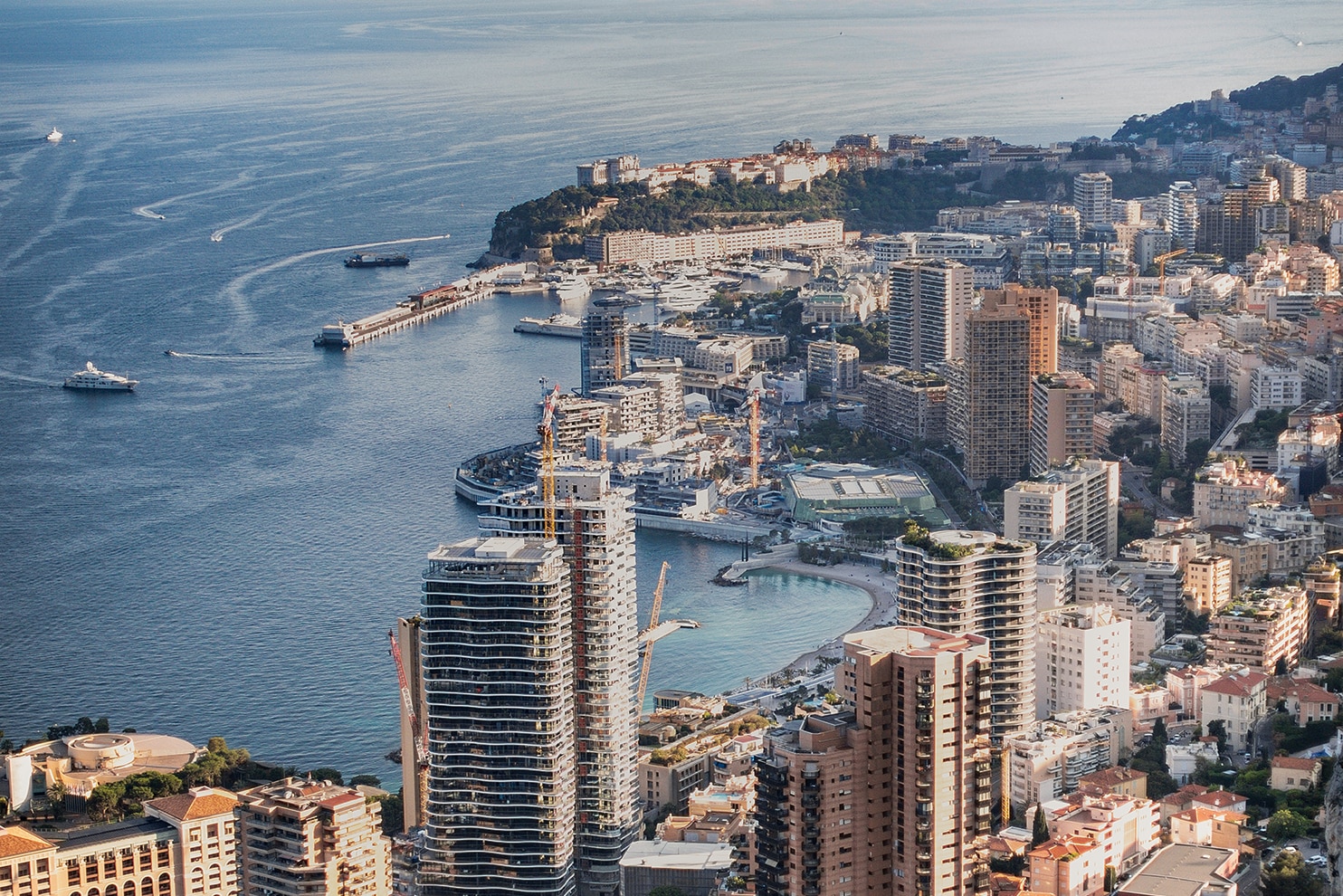 Aerial view of Monaco’s coastal skyline with high-rise buildings and a busy harbor on the Mediterranean.
