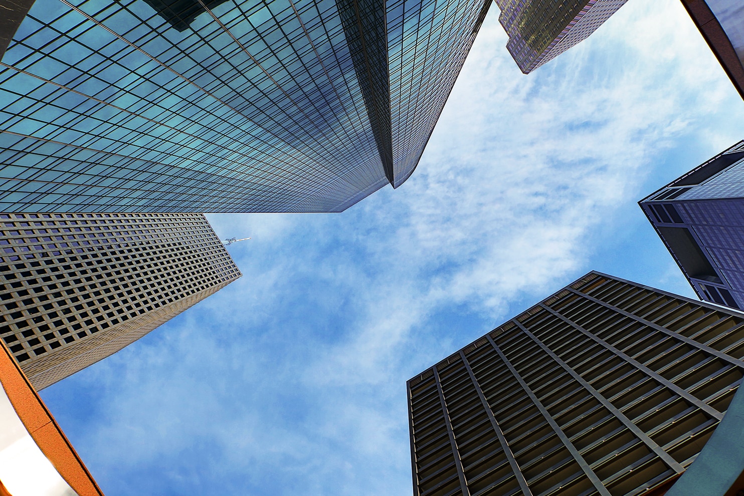An urban scene with modern glass skyscrapers reflecting the sky and surrounding buildings. The foreground features a busy intersection with cars, pedestrians, and street signs. A large white building with a grid-like facade stands prominently, while a mix of contemporary and older architecture adds depth to the cityscape