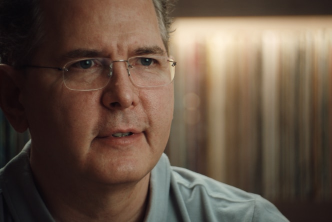 Craig Kallman, wearing a light-colored shirt, looks focused while speaking, with a background of blurred books or records.