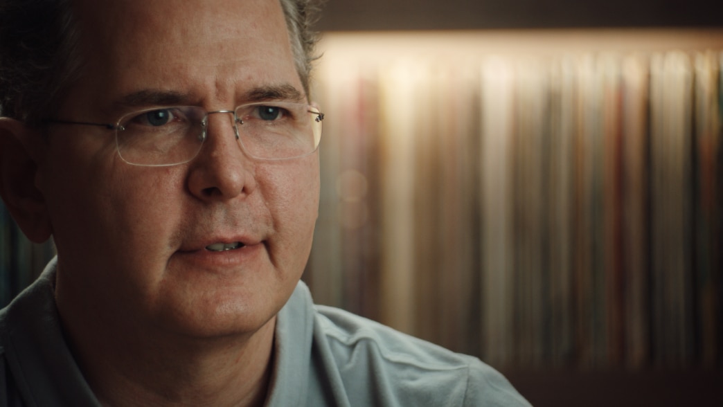 Craig Kallman, wearing a light-colored shirt, looks focused while speaking, with a background of blurred books or records.
