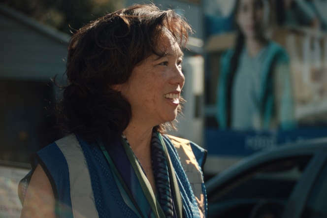 Kathy Kwan wears a reflective safety vest and a scarf smiles while standing outdoors. 