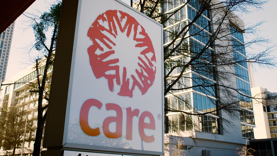 A large outdoor sign with the red Care logo and name, set against a glass office building.