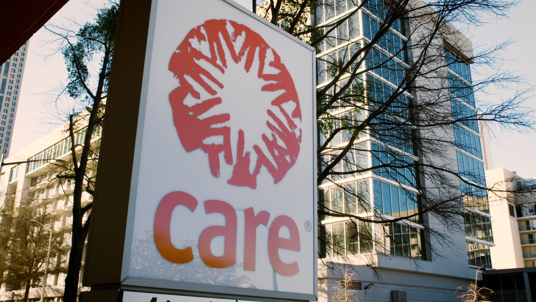 A large outdoor sign with the red Care logo and name, set against a glass office building.
