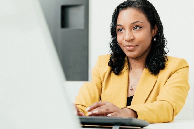 Woman in yellow blazer working on a computer.