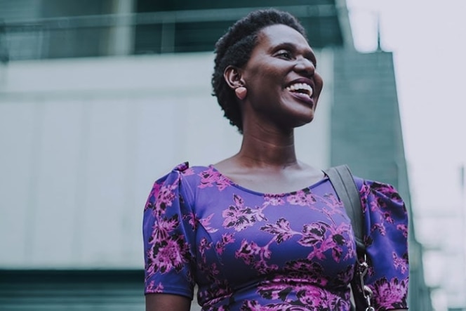 Smiling woman in a purple floral dress standing outdoors.