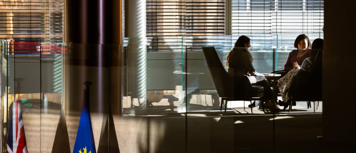 Group of women having a meeting in a sunlit glass-walled office.