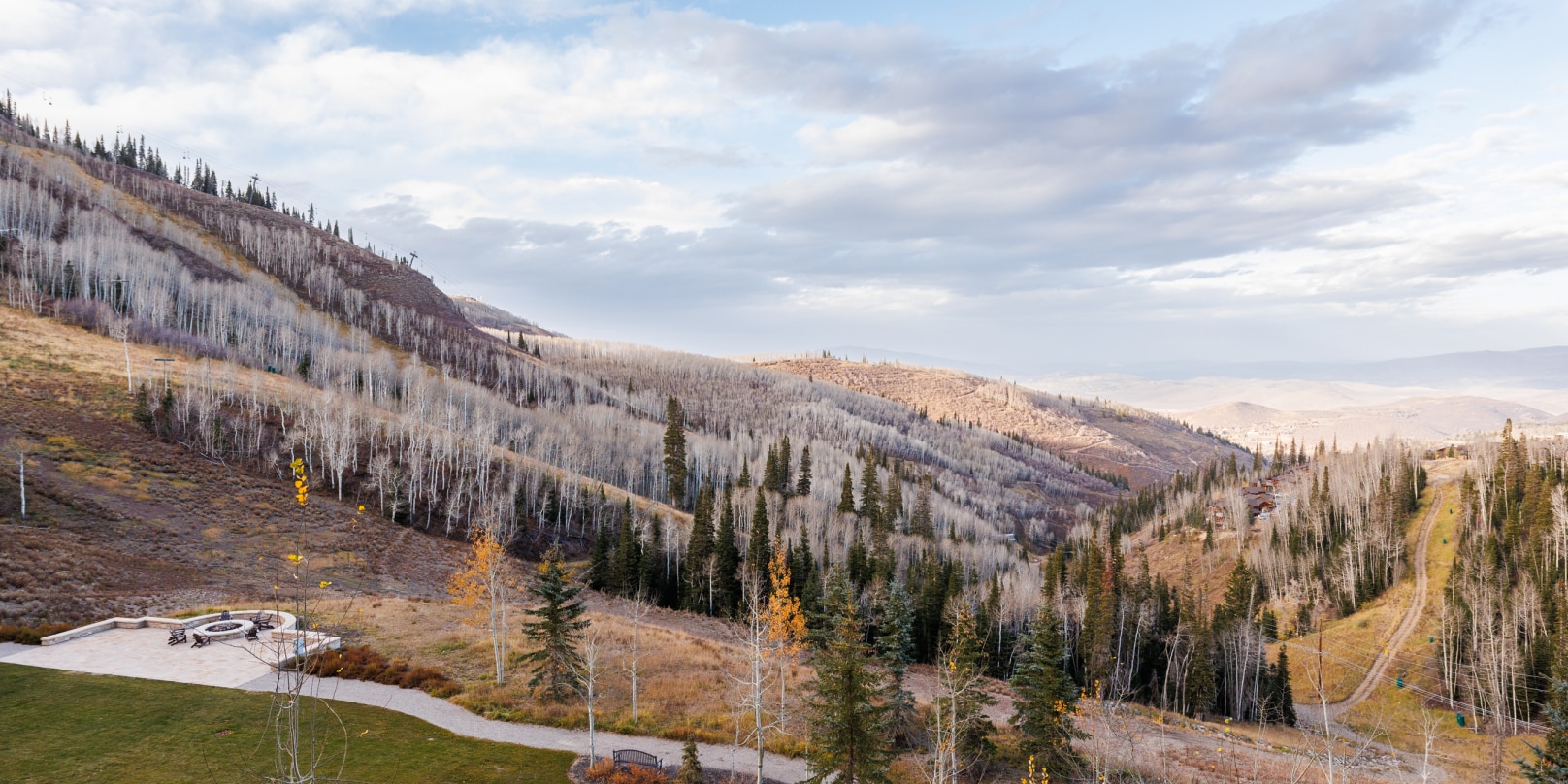 An expansive view of mountainous terrain with trees overlooking an empty campsite.