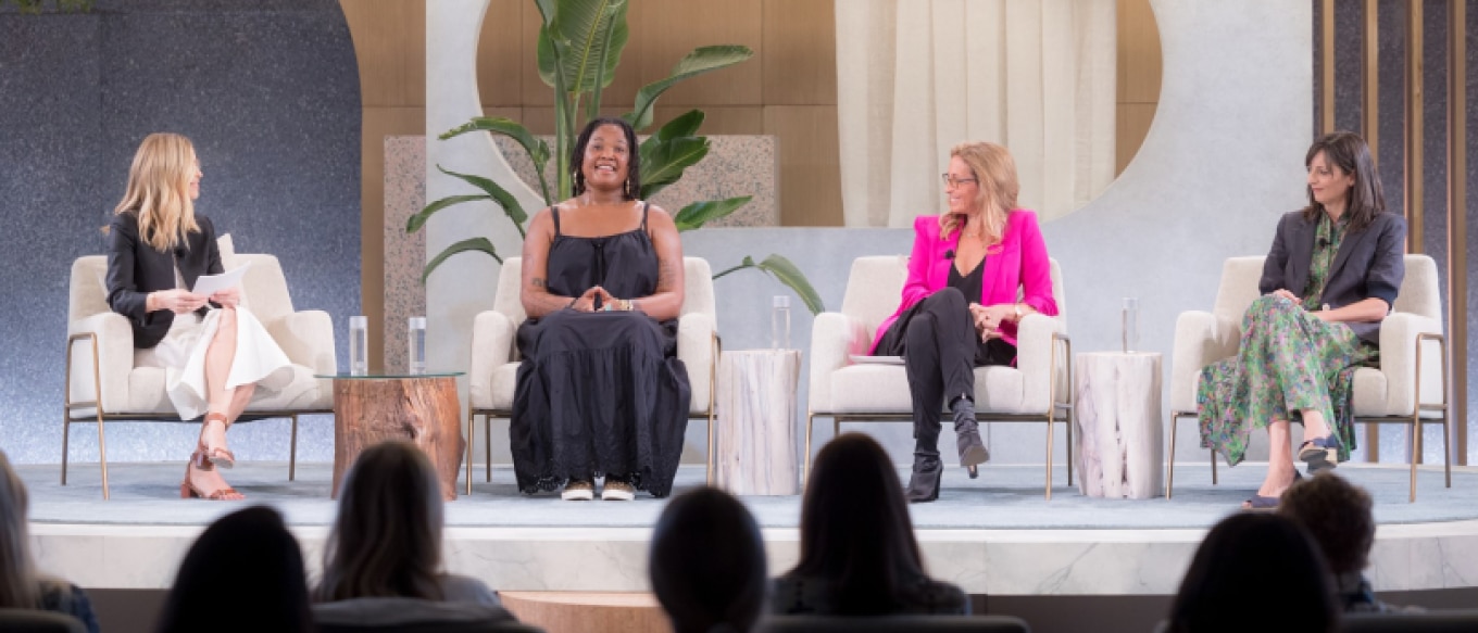 Four women seated on a stage participating in a panel discussion in front of an audience. From left to right: Fiona Carter, Beatrice Dixon, Jessica Goldman Srebnick, and Sarah Harden. The setting features modern decor with neutral tones, plants, and wooden accent tables. Each panelist is dressed stylishly, with a professional yet relaxed atmosphere.