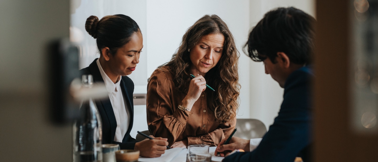 A small group of people viewed through a doorway are discussing some documents laid on a table top.