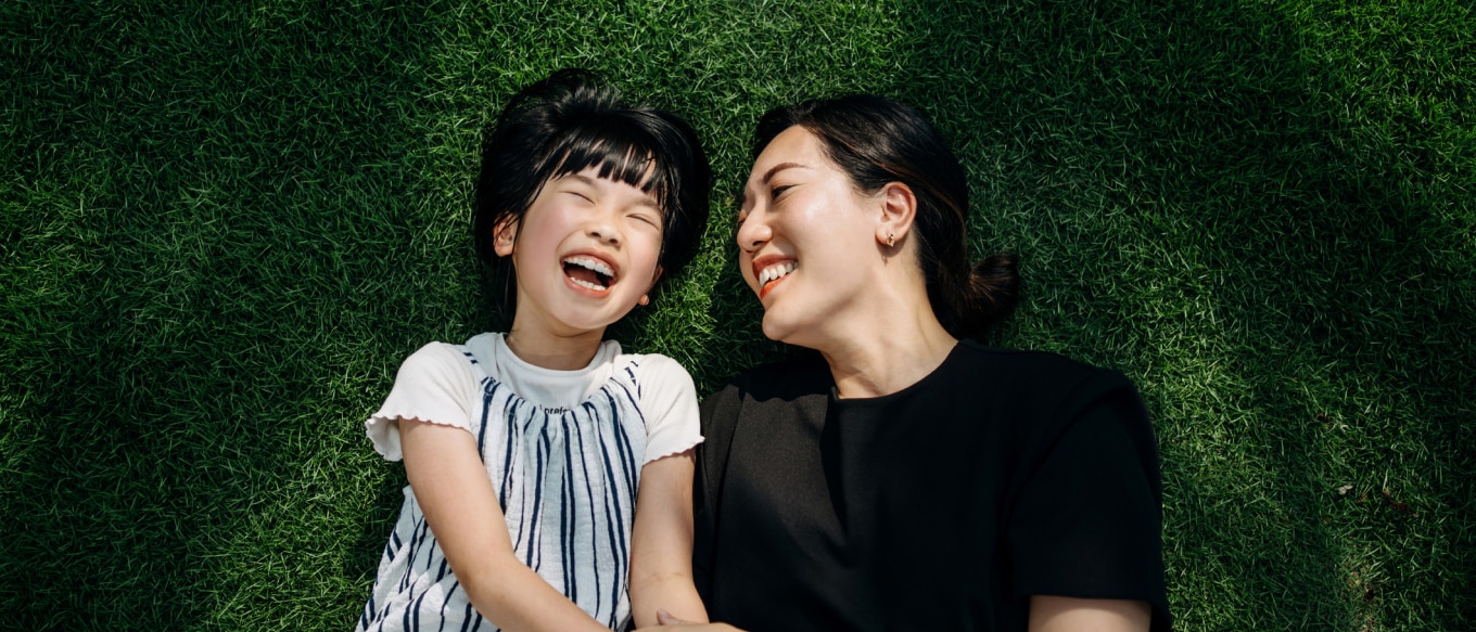 Mother and daughter laying in grass laughing