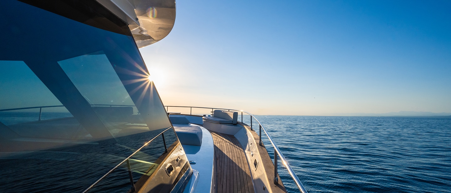 Three professionals sit at a modern table in a well-lit office with large windows. A woman in a suit takes notes while a man in glasses and a woman in a blouse listen attentively, holding coffee cups. A vase with flowers sits on the table.