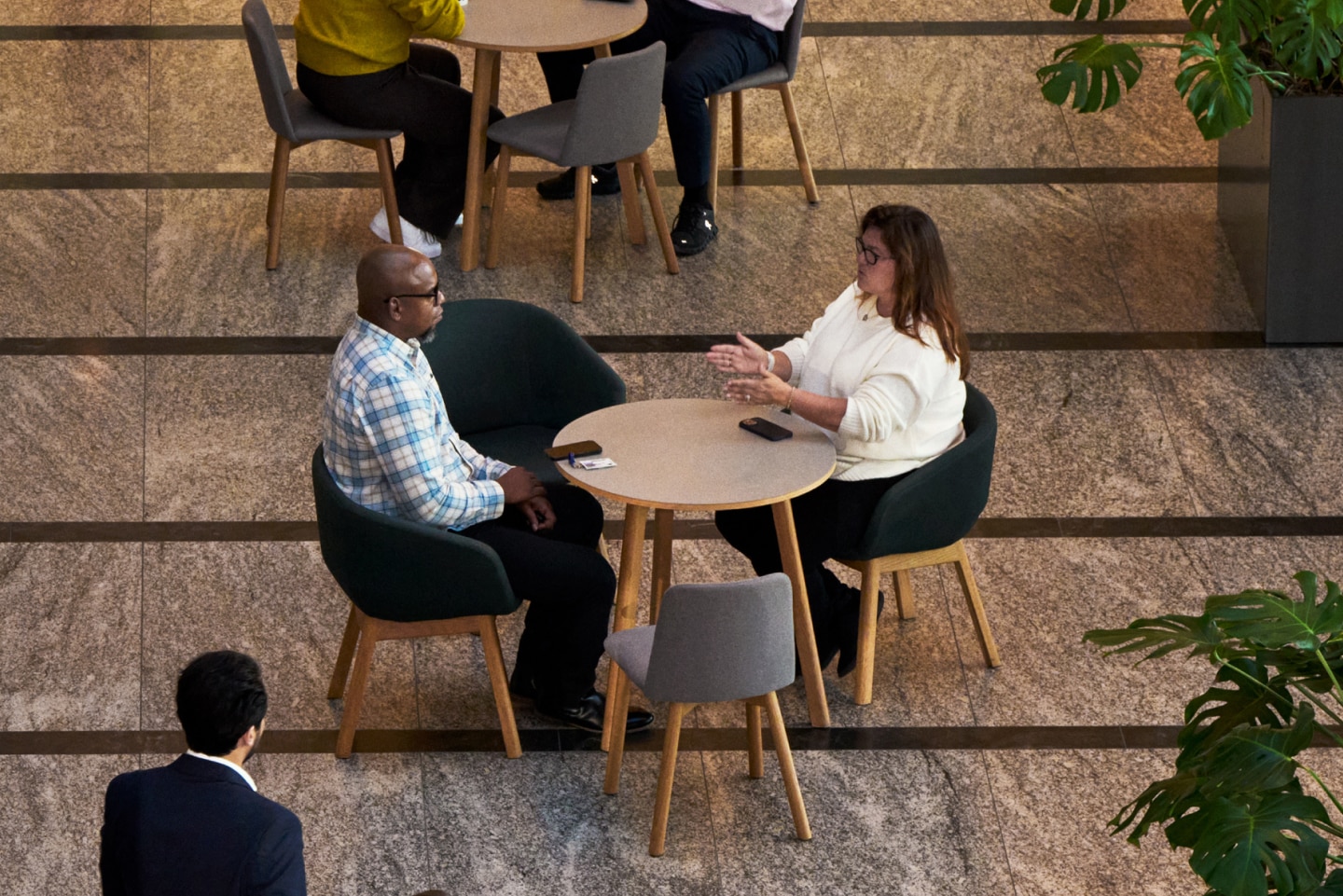 Two colleagues have a conversation at a round table in a modern office lobby.