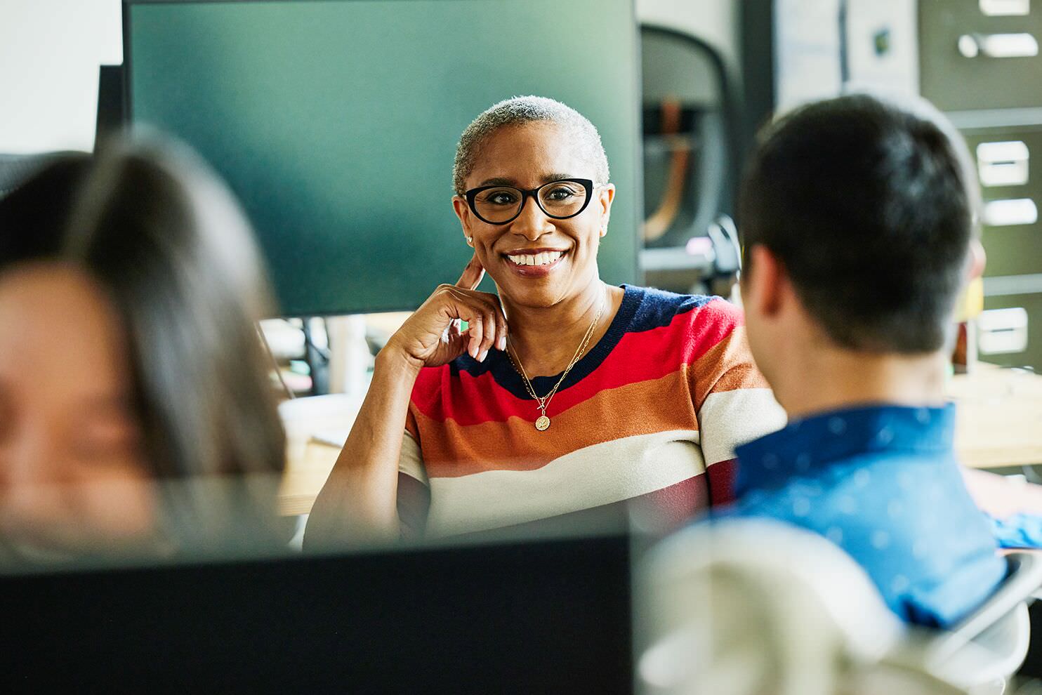 Smiling professional engages in conversation with colleagues in a modern office setting.
