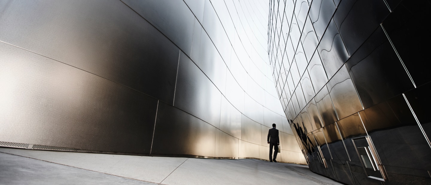 A businessman in a suit walks between two sleek, reflective metal buildings with curved surfaces
