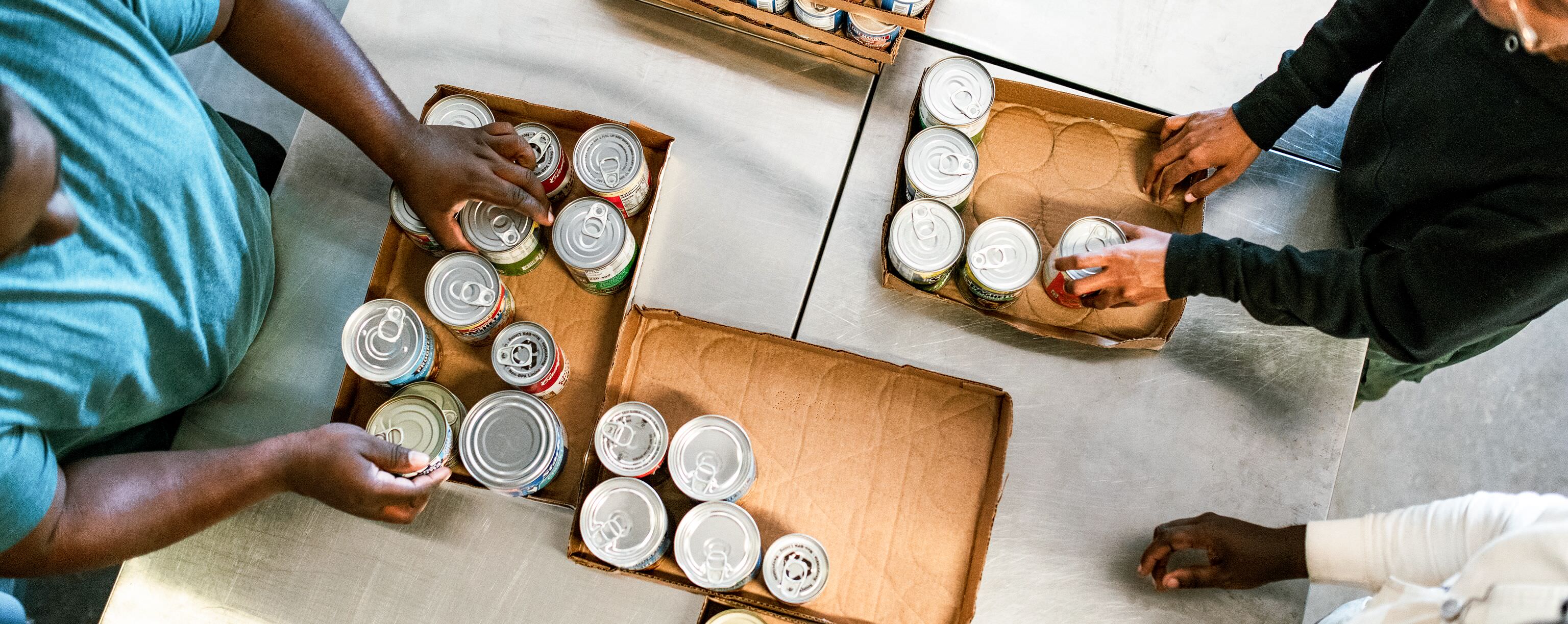Volunteers sort canned goods into cardboard trays at a food bank or community service center